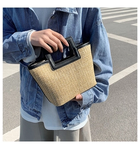 Detail of woven straw tote bag featuring black leather handles and trapezoid structure