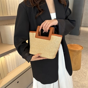Detail of woven straw tote bag with brown faux leather handles and textured fiber finish