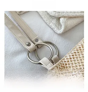 Detail showing the light leather strap connected with circular metal hardware on a straw tote