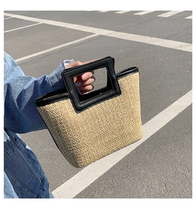 Close-up of woven straw tote bag featuring black leather handles and trim detail