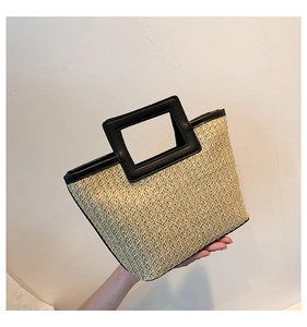 Detail of woven straw tote bag featuring black resin handles and sleek leather trim