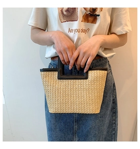 Detail of woven straw tote bag with black leather handle and trapezoid structure