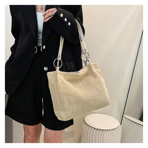 Detail of large woven straw tote bag featuring creamy leather straps and silver ring hardware