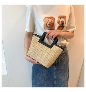Detail of woven straw tote bag with black leather handles shown on a female model