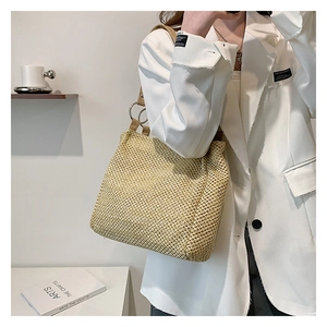 Close-up of woven straw tote bag featuring leather shoulder strap and metal ring detail