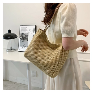 Detail of straw woven tote bag featuring a leather strap and metallic ring attachment