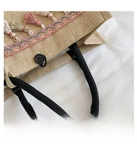 Detail of woven linen tote bag featuring pink fringe tassels and black rope handles