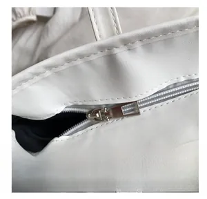 Detailed close-up of smooth metal zipper and stitching on a white leather tote bag