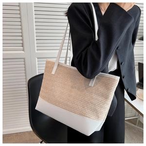 Detail of large woven straw tote bag with white leather contrast and dual shoulder straps