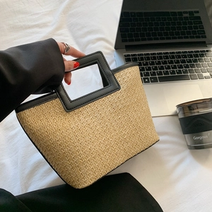 Minimalist woven straw tote bag with black contrast handles and spacious trapeze shape