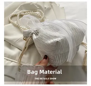 Close-up of white pleated texture fabric bucket bag with elegant pearl strap detail