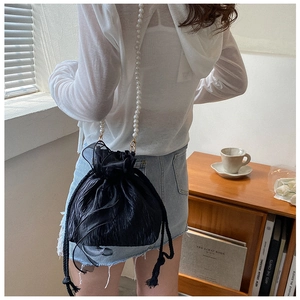 Detail of a black pleated drawstring bag with an elegant long pearl shoulder strap