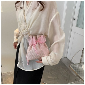Detail of pink pleated bucket bag featuring oversized lace bow and pearl beaded strap