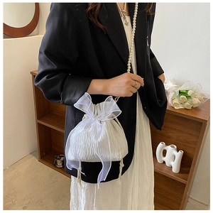 Detail of white drawstring bucket bag featuring organza bow and pearl chain strap