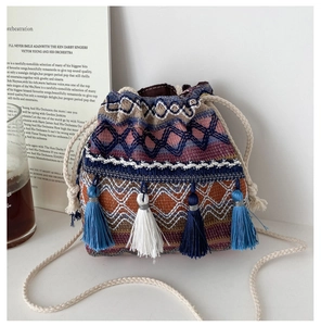 Détail du sac seau tissé bohème aux motifs géométriques colorés et pompons pendants