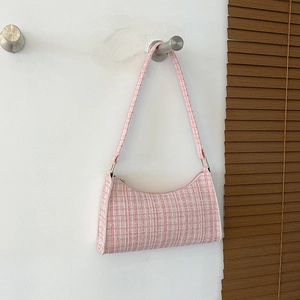 Sac à bandoulière en tweed rose et blanc suspendu sur un fond de mur blanc minimaliste