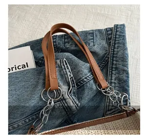 Detail of blue denim and white woven tote bag with brown leather handles and silver hardware