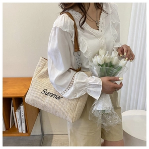 Close-up of woven straw tote bag featuring Summar embroidery and brown chain strap