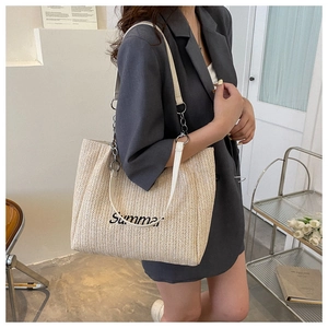 Detail of woven straw tote bag featuring Summer embroidery and dual leather chain straps