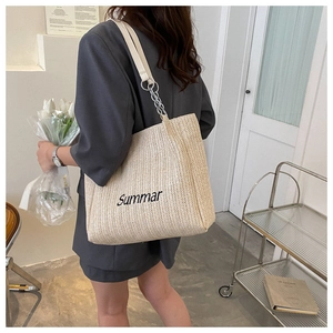 Detail of beige straw tote with Summar embroidery and metal chain shoulder strap