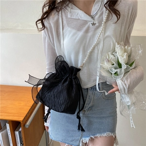 Chic black drawstring bucket bag with pearl strap and lace bow shown in a lifestyle setting