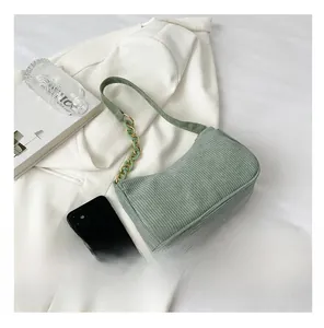 Size comparison of green corduroy baguette bag with chain strap next to a smartphone