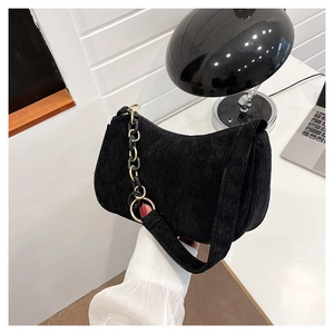 Detail of black corduroy underarm bag featuring a gold chain and textured fabric finish