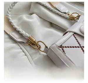 Close-up of golden metal hooks and woven leather strap on a quilted white handbag
