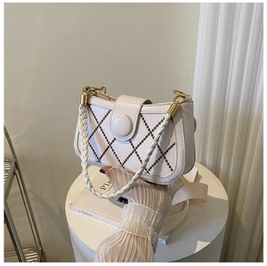 Detail of white quilted crossbody bag with woven handle and gold metal hardware