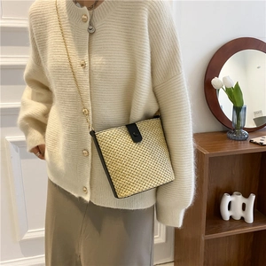 Minimalistische stro emmer tas met lederen gesp en gouden ketting gedragen door een model