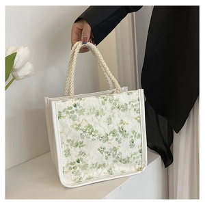 Detail of white tote bag featuring green floral lace overlay and woven rope handles
