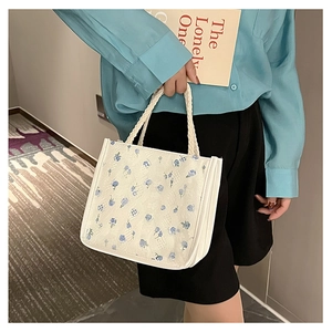 Detail of blue floral embroidery and woven rope handle on a white canvas tote bag