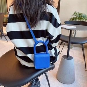 Detalle del mini bolso bandolera azul Klein con asa superior sobre un suéter de rayas