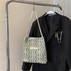 Dettaglio della borsa a tracolla intrecciata verde e beige con etichetta in pelle