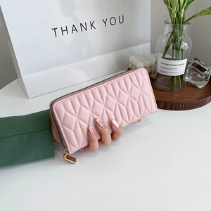 Pink quilted leather clutch wallet with gold zipper detail held in hand for scale