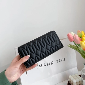Close-up of black quilted long wallet with golden zipper detail held in hand