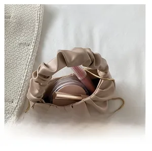 Detail view of beige ruched cloud bag interior with gold chain strap and cosmetics