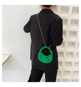 Close-up of grass green ruched cloud bag with gold chain strap on black blazer