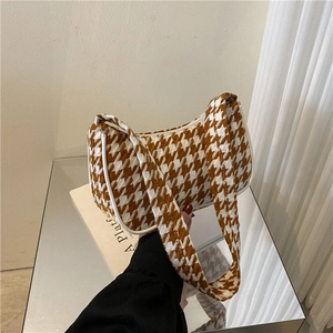 Detailopname van de houndstooth-textuur en schouderband van een vintage baguette-tas