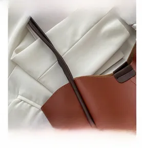 Detail of brown leather tote bag handle and textured surface on a white blazer