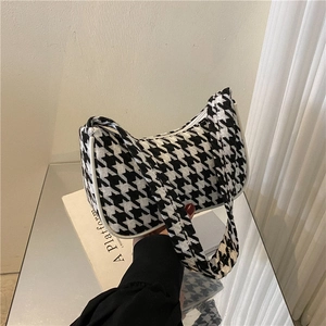 Detailopname van houndstooth baguette tas met focus op textuur en witte biesjes
