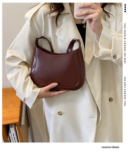 Detail of a burgundy patent leather hobo bag worn with a chic beige trench coat