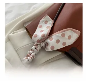 Detail of a brown leather tote bag handle decorated with a pink polka dot silk scarf