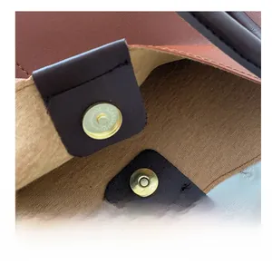 Close-up of brass magnetic clasp and pebbled leather texture on brown tote bag