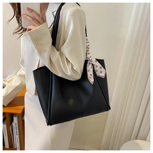 Detail of black leather tote bag featuring elegant polka dot silk scarf on the handle