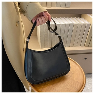 Minimalist black leather crescent underarm bag shown on a wooden stool in a cozy interior