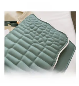 Macro detail of sage green alligator embossed leather texture with white contrast piping