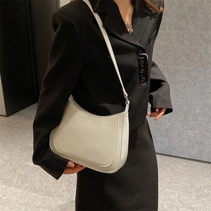 Minimalist cream shoulder bag with curved base worn by a model in a black blazer suit