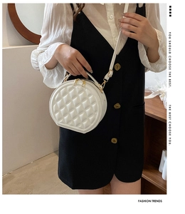 Close-up of white round quilted crossbody bag with golden hardware and embroidery detail