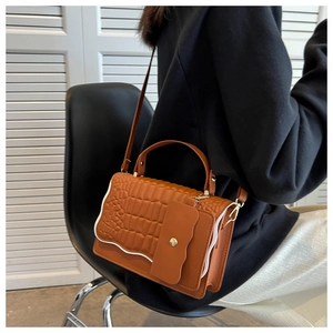 Detail of brown crocodile pattern handbag with white wavy trim and gold metal buckle
